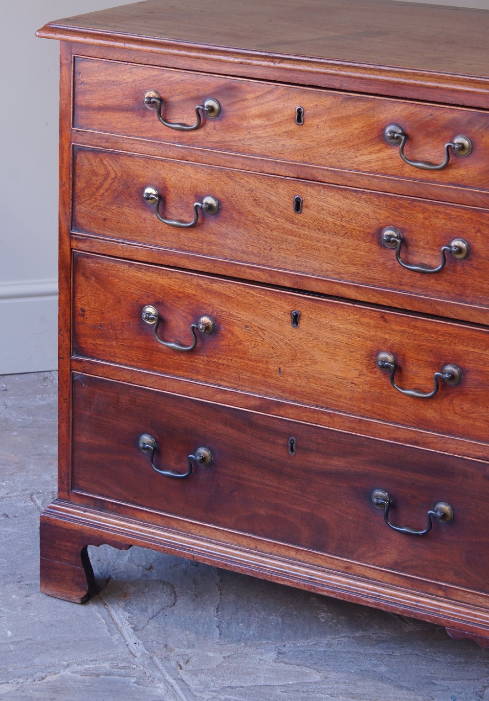 An 18th-century Georgian mahogany chest of drawers featuring four graduated drawers, brass swan-neck handles, keyhole escutcheons, and bracket feet. View III