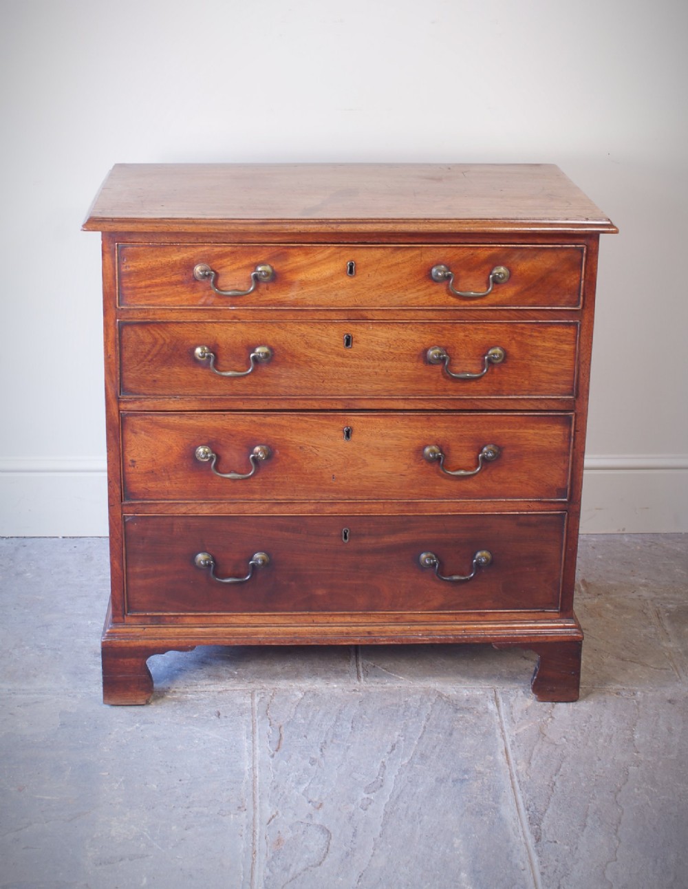 An 18th-century Georgian mahogany chest of drawers featuring four graduated drawers, brass swan-neck handles, keyhole escutcheons, and bracket feet. View XIV