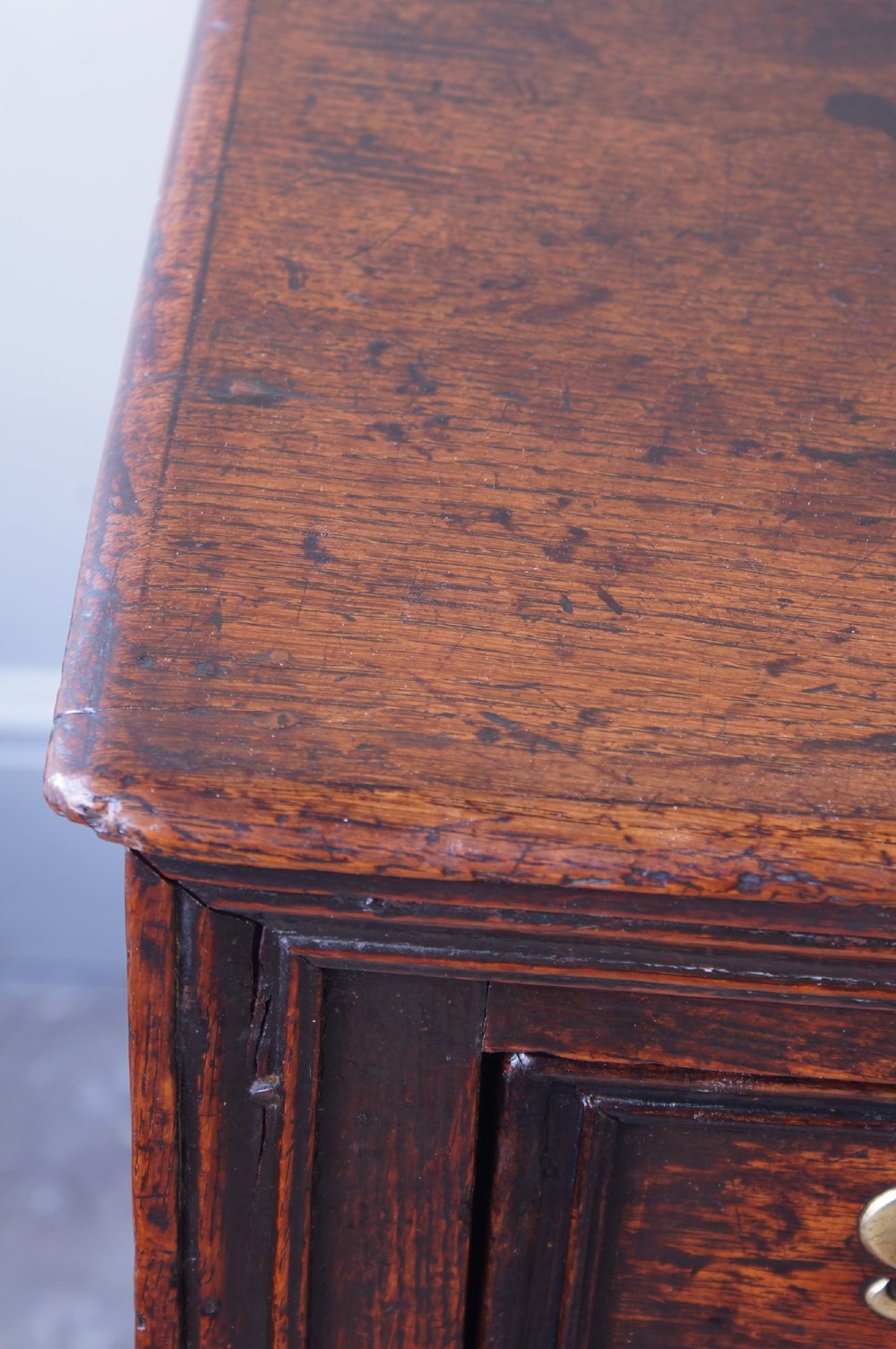 A 17th-century dark oak dresser base featuring three drawers above panelled cupboard doors with geometric moulding and brass drop handles. View VIII