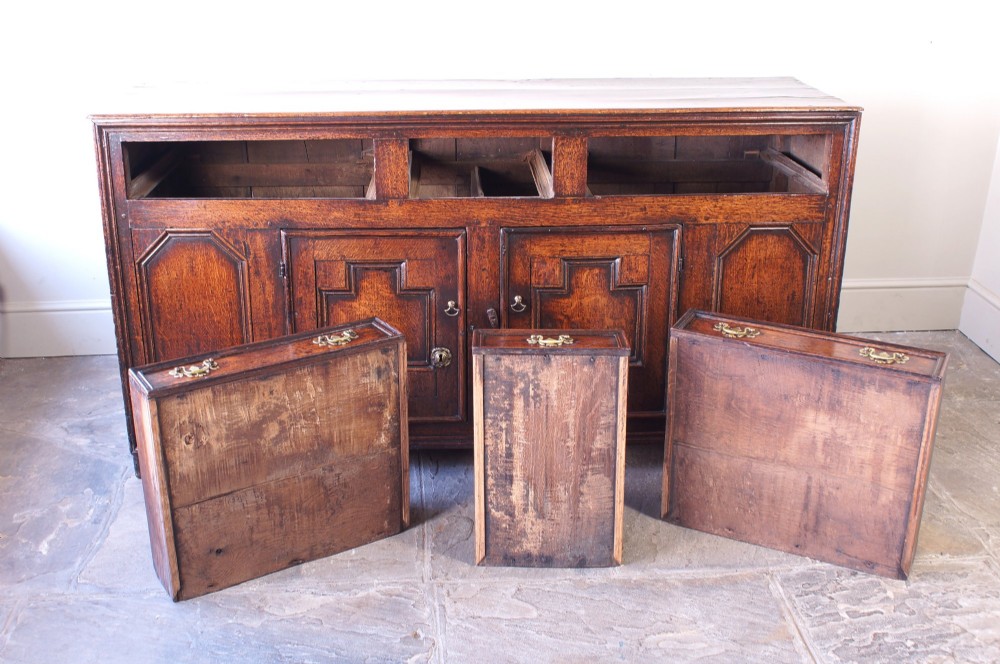 A 17th-century dark oak dresser base featuring three drawers above panelled cupboard doors with geometric moulding and brass drop handles. View IX