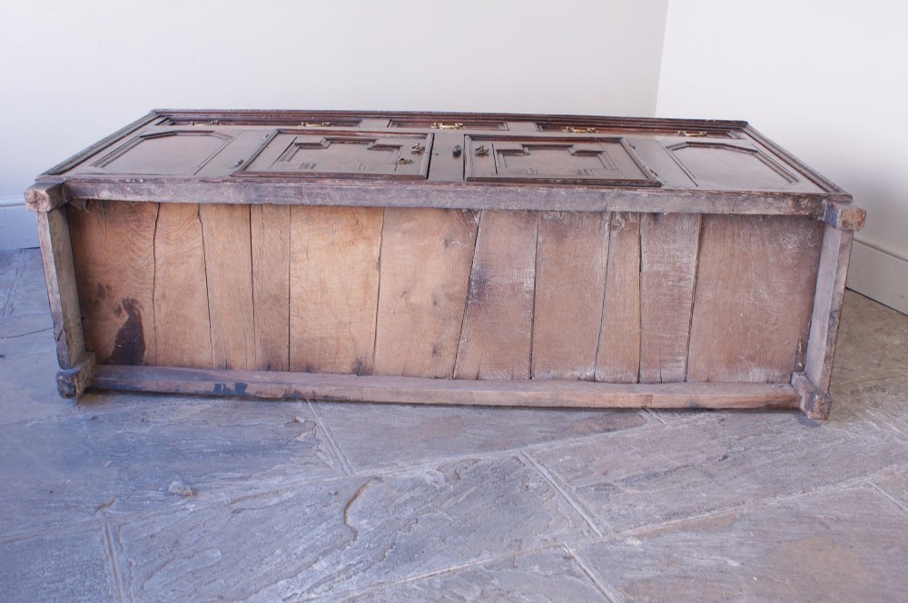 A 17th-century dark oak dresser base featuring three drawers above panelled cupboard doors with geometric moulding and brass drop handles. View XI