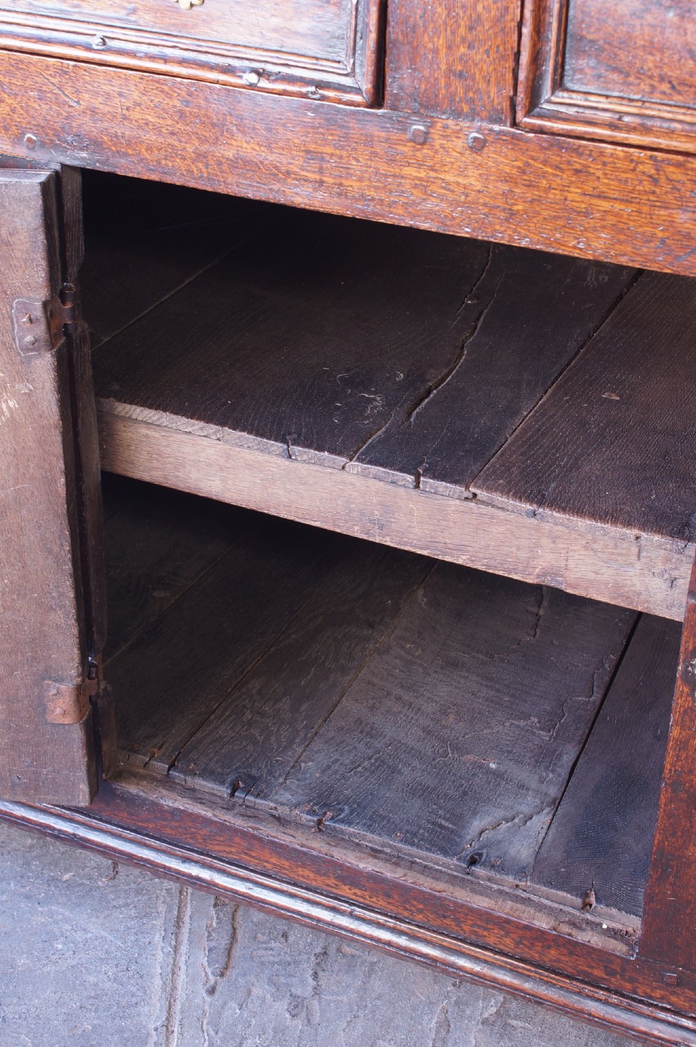 A 17th-century dark oak dresser base featuring three drawers above panelled cupboard doors with geometric moulding and brass drop handles. View XII