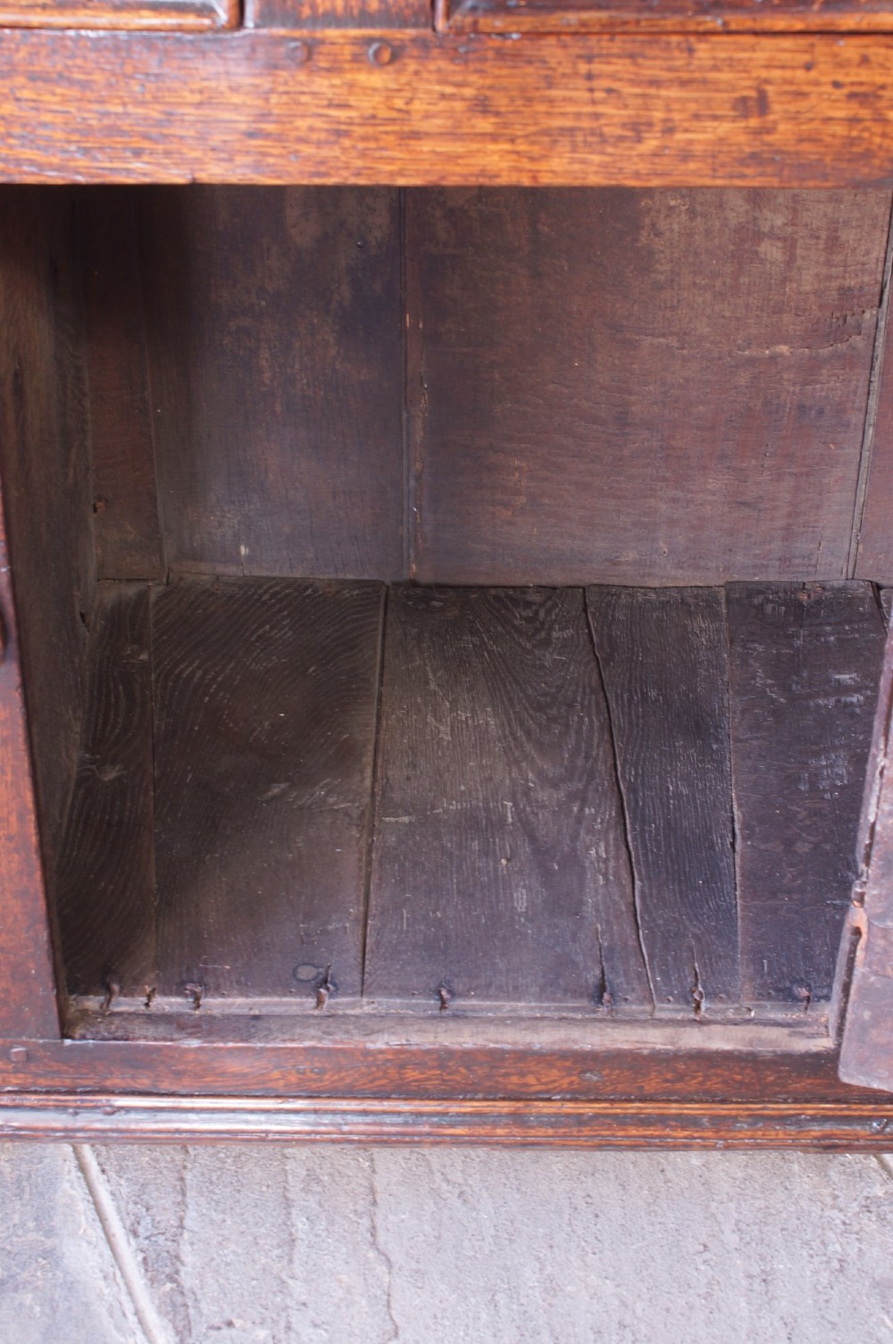 A 17th-century dark oak dresser base featuring three drawers above panelled cupboard doors with geometric moulding and brass drop handles. View XIII