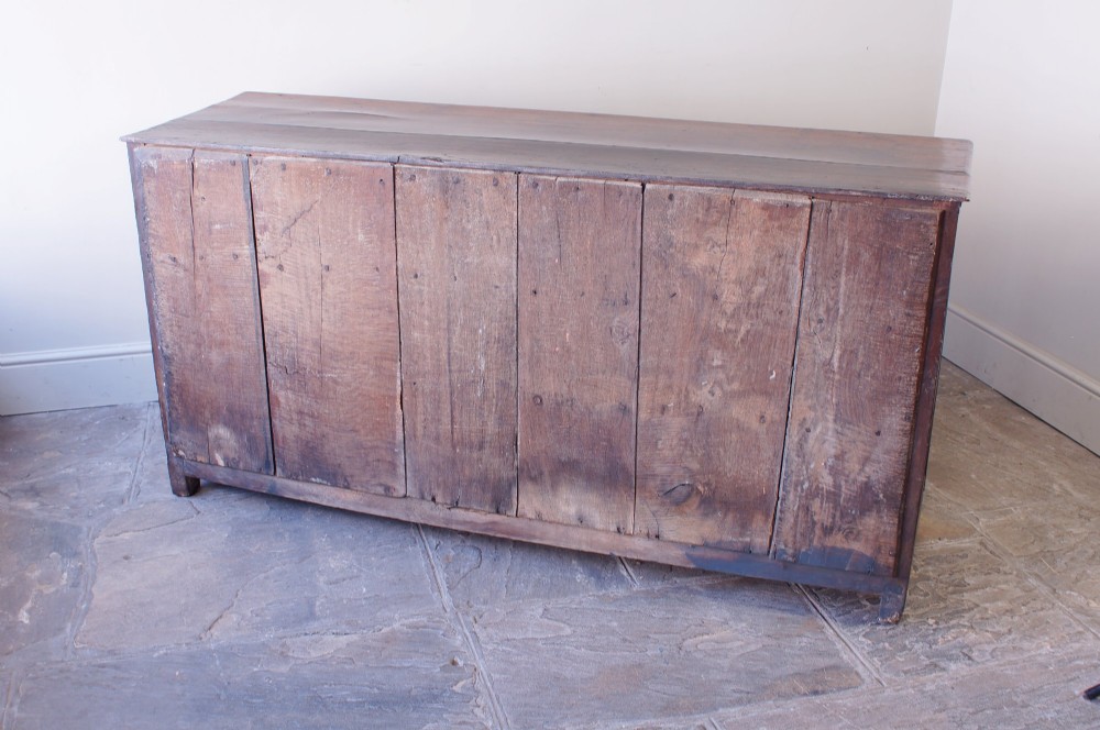 A 17th-century dark oak dresser base featuring three drawers above panelled cupboard doors with geometric moulding and brass drop handles. View XV