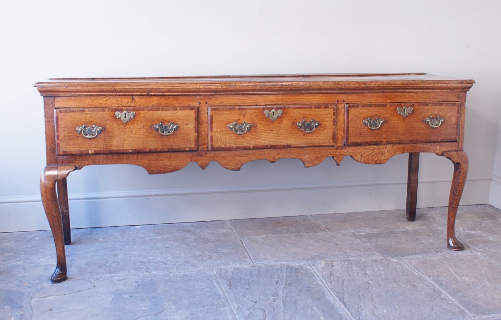 An eighteenth-century oak dresser base featuring three crossbanded drawers with brass handles, a shaped scalloped apron, and slender cabriole legs. View II