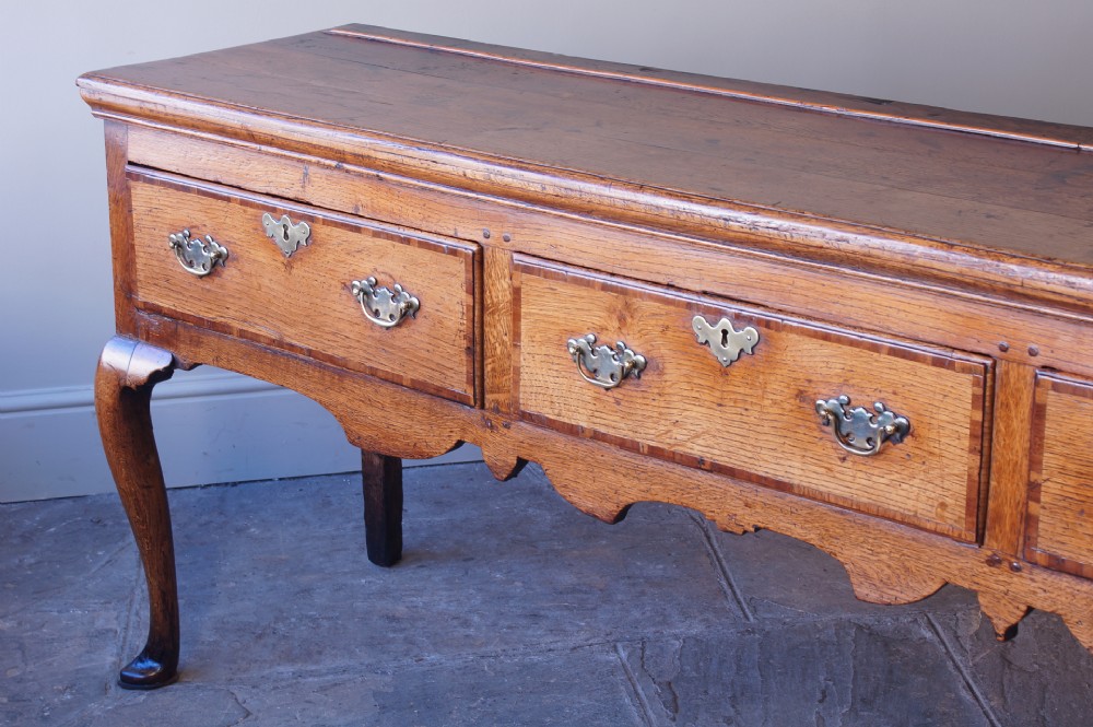 An eighteenth-century oak dresser base featuring three crossbanded drawers with brass handles, a shaped scalloped apron, and slender cabriole legs. View III