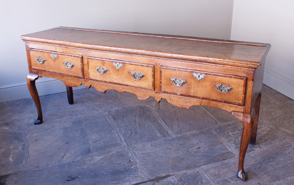 An eighteenth-century oak dresser base featuring three crossbanded drawers with brass handles, a shaped scalloped apron, and slender cabriole legs. View IV