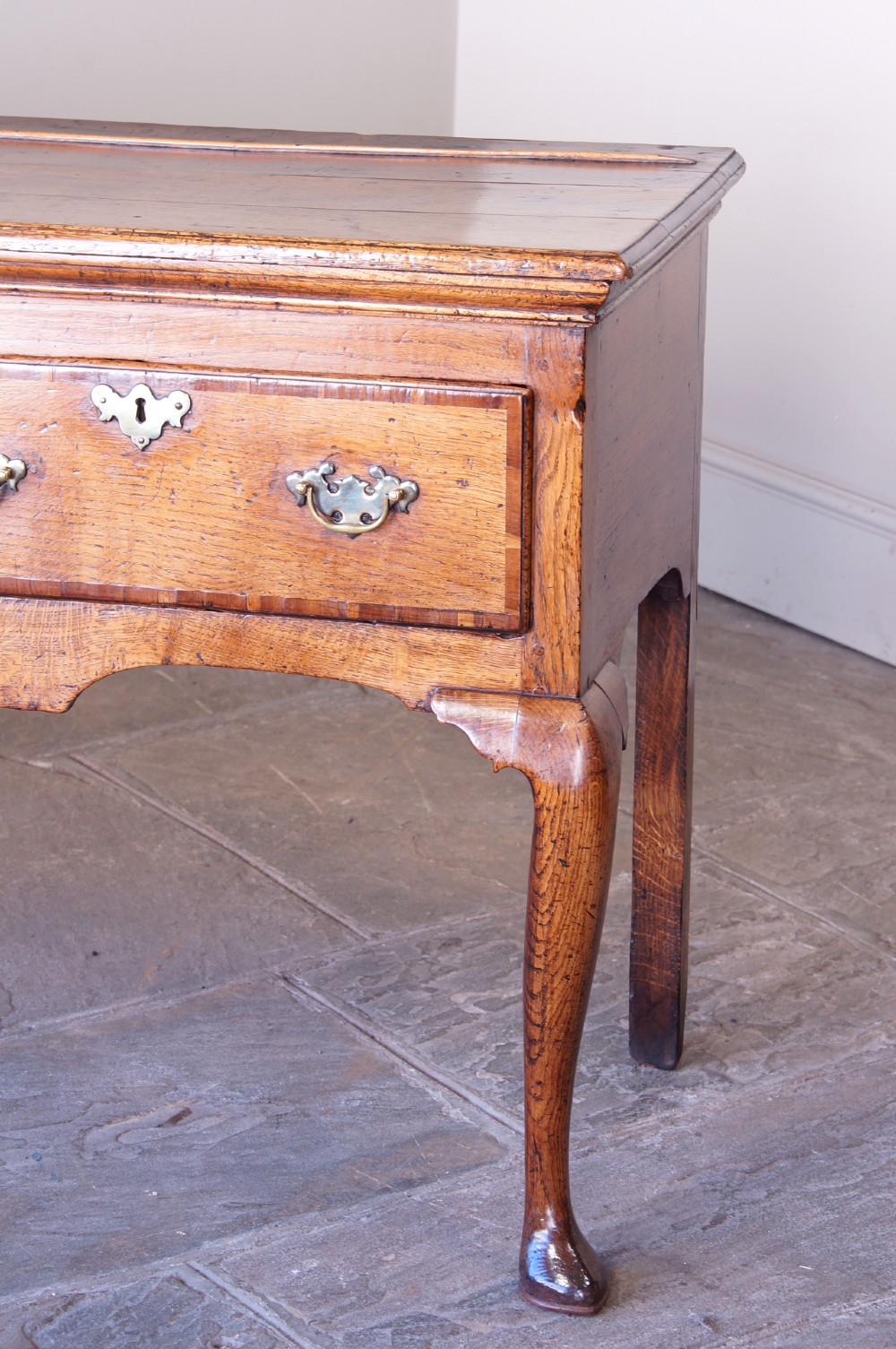 An eighteenth-century oak dresser base featuring three crossbanded drawers with brass handles, a shaped scalloped apron, and slender cabriole legs. View V