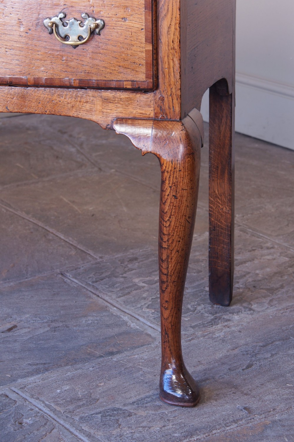 An eighteenth-century oak dresser base featuring three crossbanded drawers with brass handles, a shaped scalloped apron, and slender cabriole legs. View VII