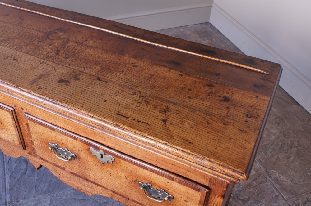 An eighteenth-century oak dresser base featuring three crossbanded drawers with brass handles, a shaped scalloped apron, and slender cabriole legs. View VIII