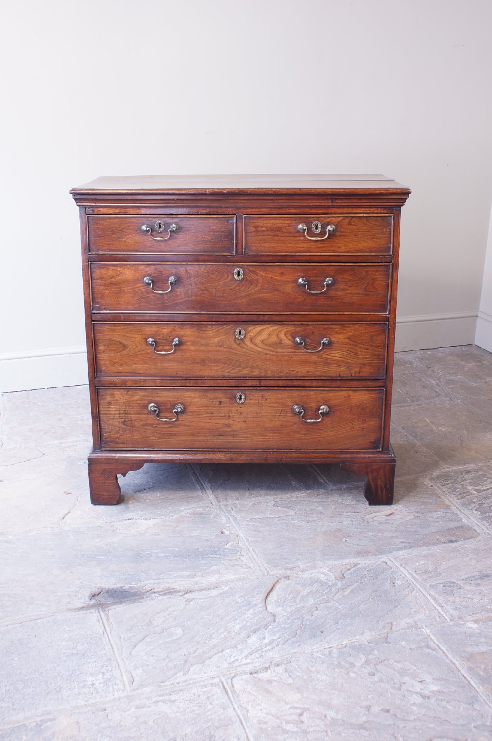 An eighteenth-century fruitwood chest of drawers with two short over three long graduated drawers, brass swan-neck handles, keyhole escutcheons, and shaped bracket feet. View II
