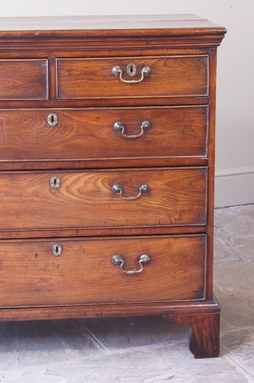 An eighteenth-century fruitwood chest of drawers with two short over three long graduated drawers, brass swan-neck handles, keyhole escutcheons, and shaped bracket feet. View III