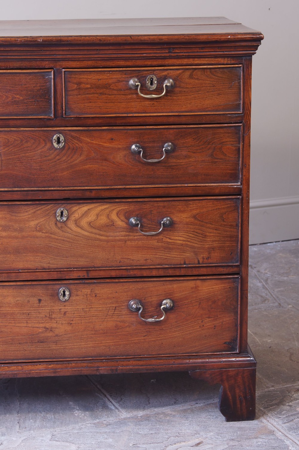 An eighteenth-century fruitwood chest of drawers with two short over three long graduated drawers, brass swan-neck handles, keyhole escutcheons, and shaped bracket feet. View IV