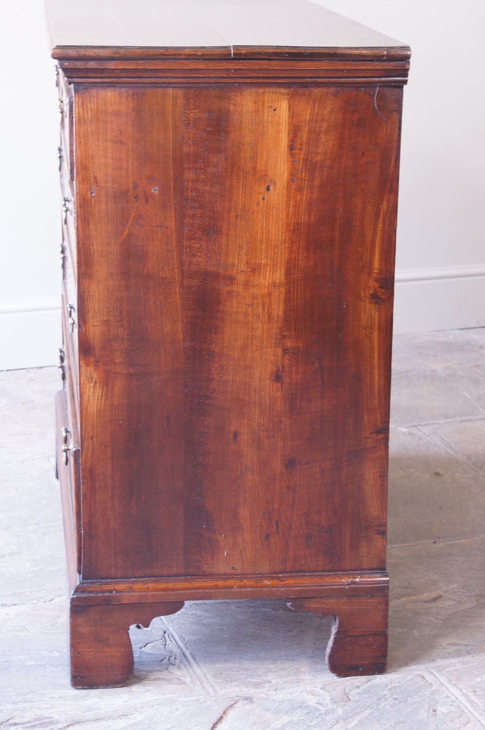 An eighteenth-century fruitwood chest of drawers with two short over three long graduated drawers, brass swan-neck handles, keyhole escutcheons, and shaped bracket feet. View VI