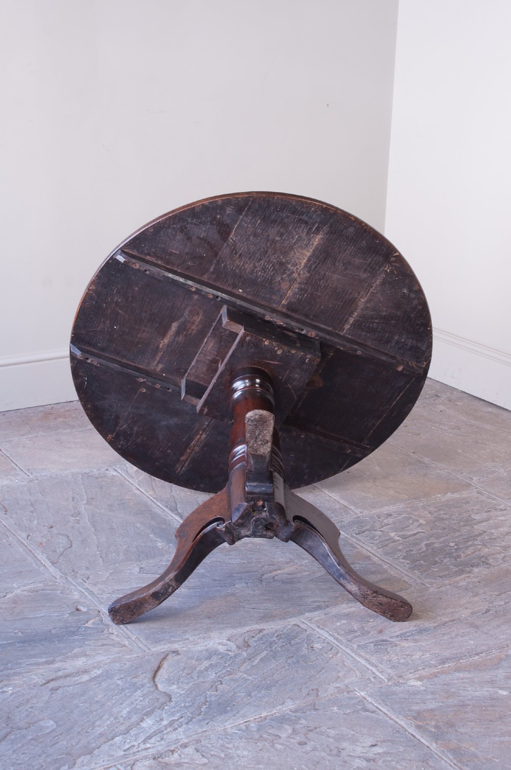 A Georgian oak tilt-top table with a circular planked top shown tilted vertically on a turned pedestal stem and tripod legs. View IV