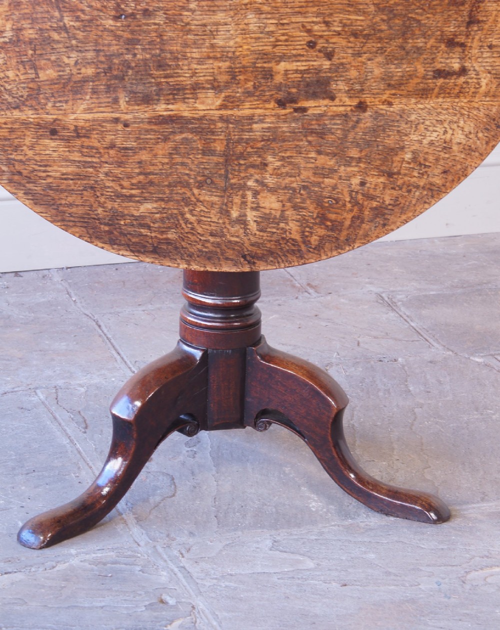 A Georgian oak tilt-top table with a circular planked top shown tilted vertically on a turned pedestal stem and tripod legs. View V