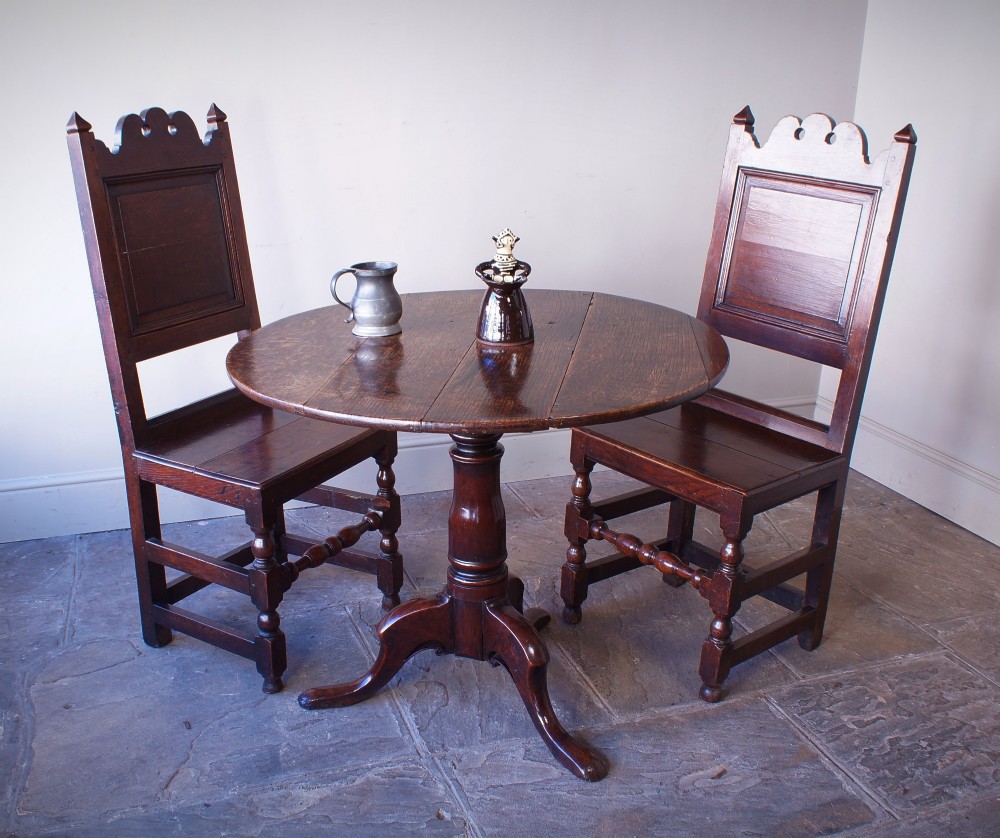 A Georgian oak tilt-top table with a circular planked top shown tilted vertically on a turned pedestal stem and tripod legs. View VI