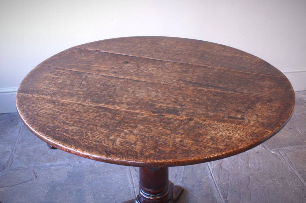 A Georgian oak tilt-top table with a circular planked top shown tilted vertically on a turned pedestal stem and tripod legs. View IX