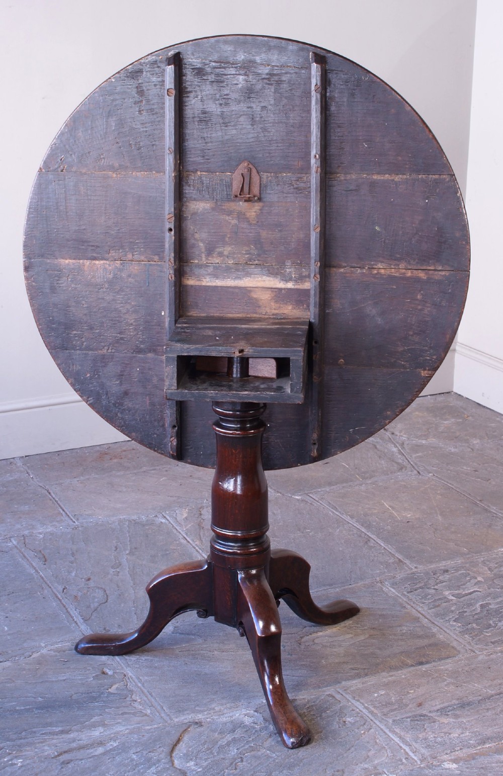 A Georgian oak tilt-top table with a circular planked top shown tilted vertically on a turned pedestal stem and tripod legs. View XI