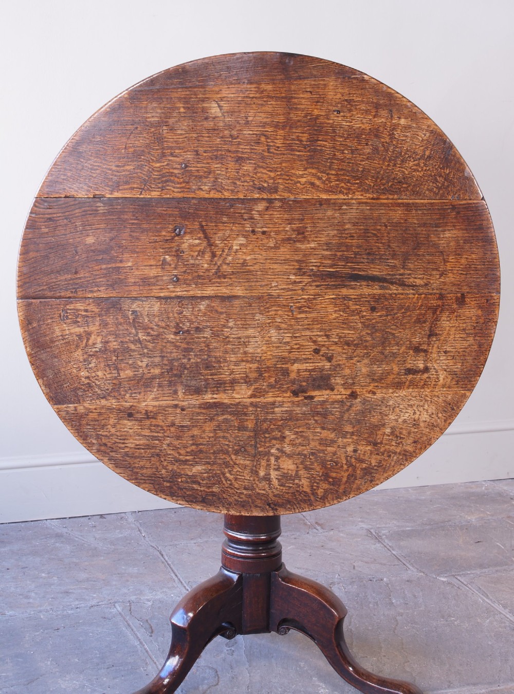 A Georgian oak tilt-top table with a circular planked top shown tilted vertically on a turned pedestal stem and tripod legs. View XIV