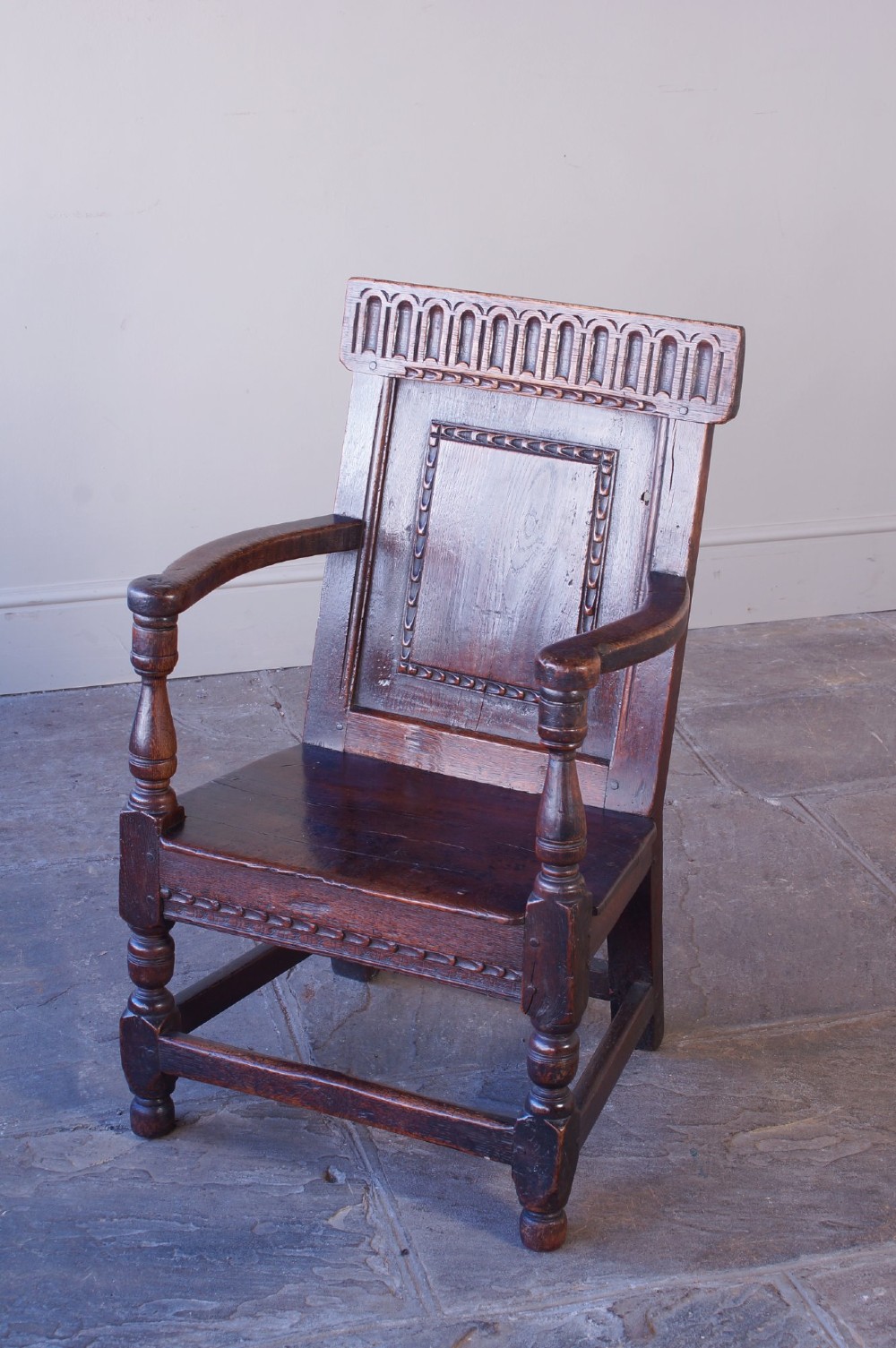 A dark brown 17th-century oak childs wainscot armchair with carved geometric back panels and turned supports. View III