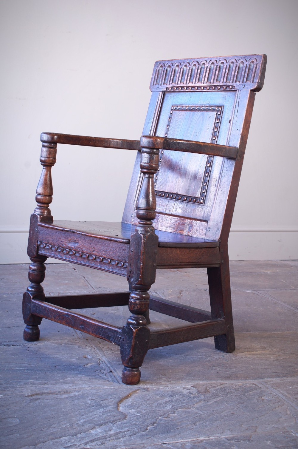 A dark brown 17th-century oak childs wainscot armchair with carved geometric back panels and turned supports. View V