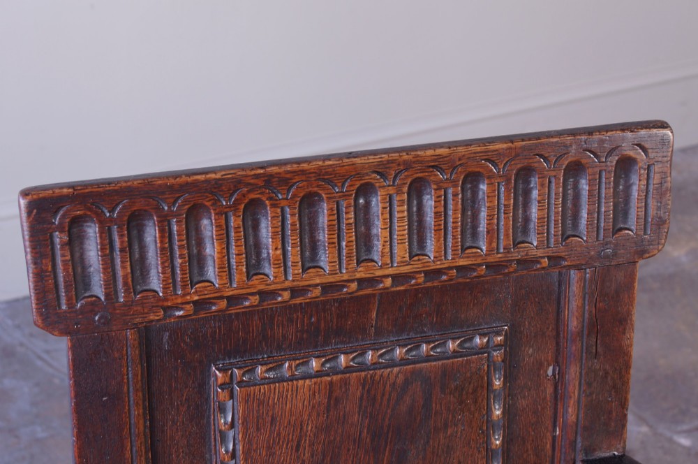 A dark brown 17th-century oak childs wainscot armchair with carved geometric back panels and turned supports. View X