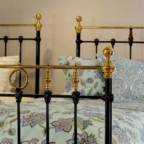 fig 2. A matching pair of black cast iron single bed frames featuring vertical spindles and polished brass top rails with decorative finials.