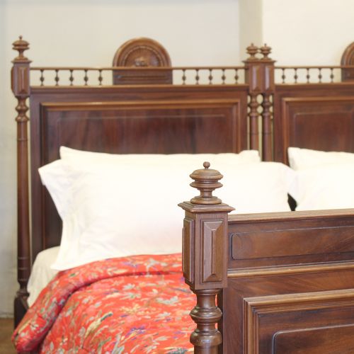 fig 2. A pair of matching nineteenth-century French mahogany single beds featuring spindled headboards and panelled footboards placed side-by-side.