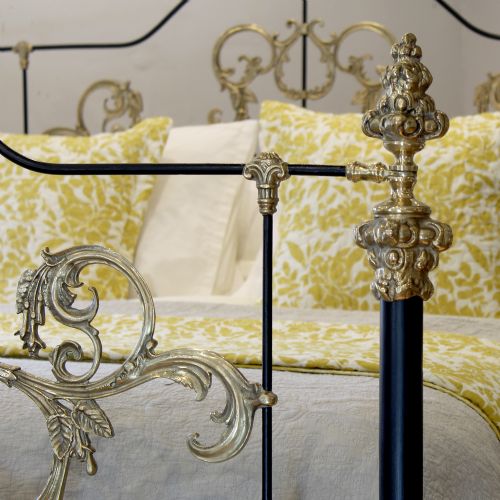 fig 1. An antique king-size bedstead featuring black cast iron posts adorned with ornate scrollwork brass embellishments and decorative finials.
