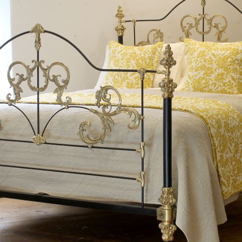 fig 2. An antique king-size bedstead featuring black cast iron posts adorned with ornate scrollwork brass embellishments and decorative finials.