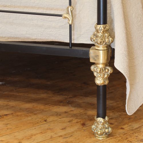 fig 3. An antique king-size bedstead featuring black cast iron posts adorned with ornate scrollwork brass embellishments and decorative finials.