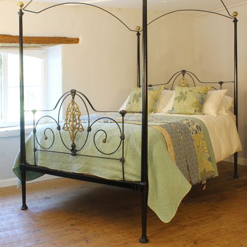 fig 1. A king size Victorian black iron four poster bed featuring arched top canopy bars, decorative brass finials, and intricate cast brass scrollwork on the headboard and footboard.