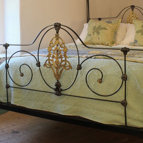 fig 2. A king size Victorian black iron four poster bed featuring arched top canopy bars, decorative brass finials, and intricate cast brass scrollwork on the headboard and footboard.