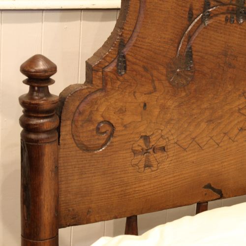 fig 1. A rustic solid oak single bed frame with a carved arched headboard and turned finials on the footboard corner posts.