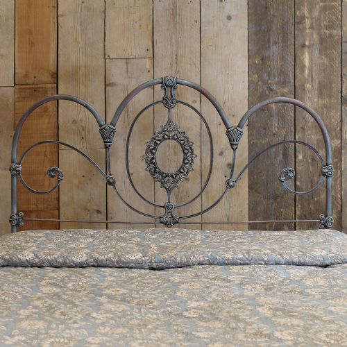 fig 1. A double metal bed frame featuring an ornate wrought iron headboard with scrollwork detail and a distressed blue verdigris painted finish.