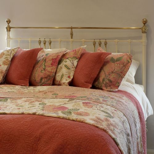 fig 1. An antique cream-painted iron bed frame featuring a brass top rail and decorative brass finials.