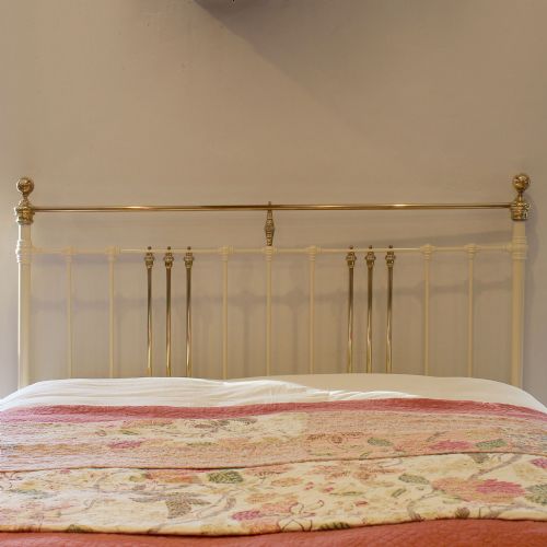 fig 2. An antique cream-painted iron bed frame featuring a brass top rail and decorative brass finials.