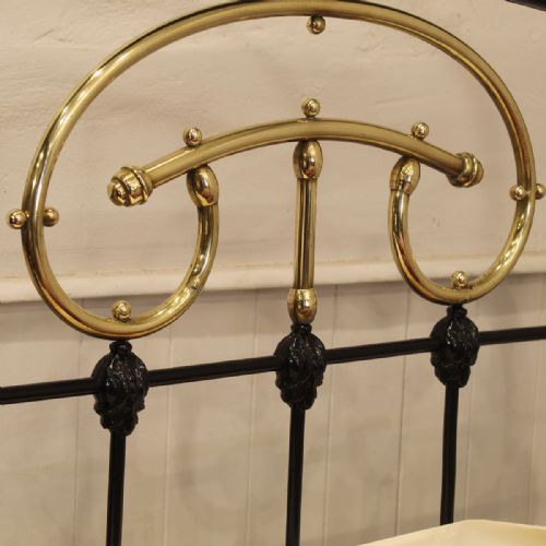 fig 1. A single Victorian black painted iron bedstead featuring decorative brass scrollwork across the curved top rails of the headboard and footboard.