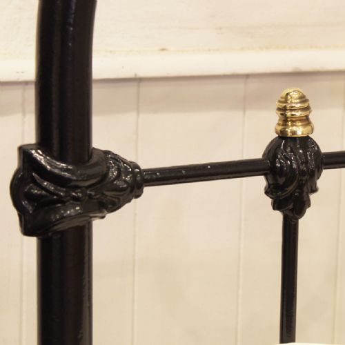 fig 2. A single Victorian black painted iron bedstead featuring decorative brass scrollwork across the curved top rails of the headboard and footboard.