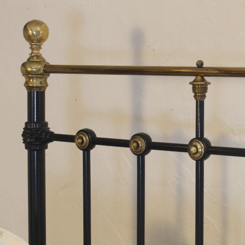 fig 1. A Victorian single bedstead featuring a black iron frame, vertical spindles, brass accent roundels, and polished brass top rails with brass finials.