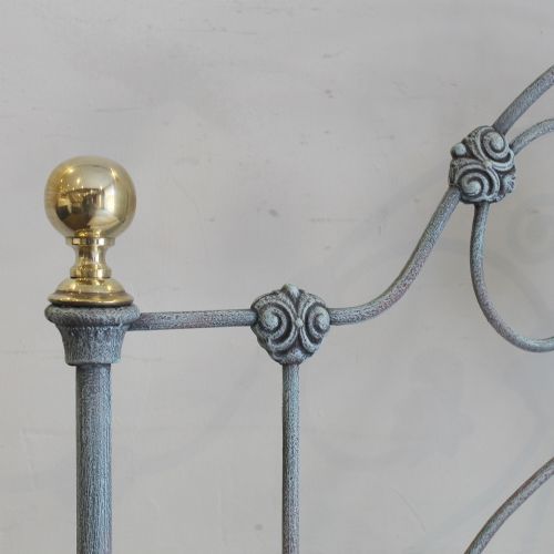 fig 1. A 3ft single antique iron bedstead featuring a light blue verdigris finish with open scrollwork and brass finials on the headboard and footboard.