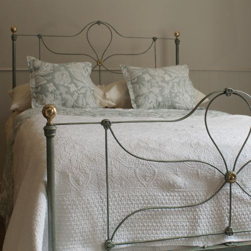 fig 1. An antique double cast iron bedstead featuring a green verdigris finish, looped wirework panels, and brass finials.