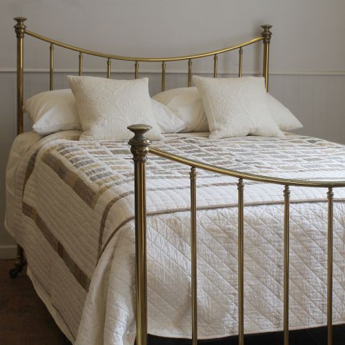 fig 1. An antique Victorian double brass bed frame featuring curved top rails, vertical tubular spindles, brass finials, and caster wheels.