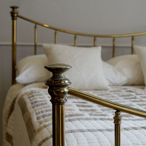 fig 2. An antique Victorian double brass bed frame featuring curved top rails, vertical tubular spindles, brass finials, and caster wheels.
