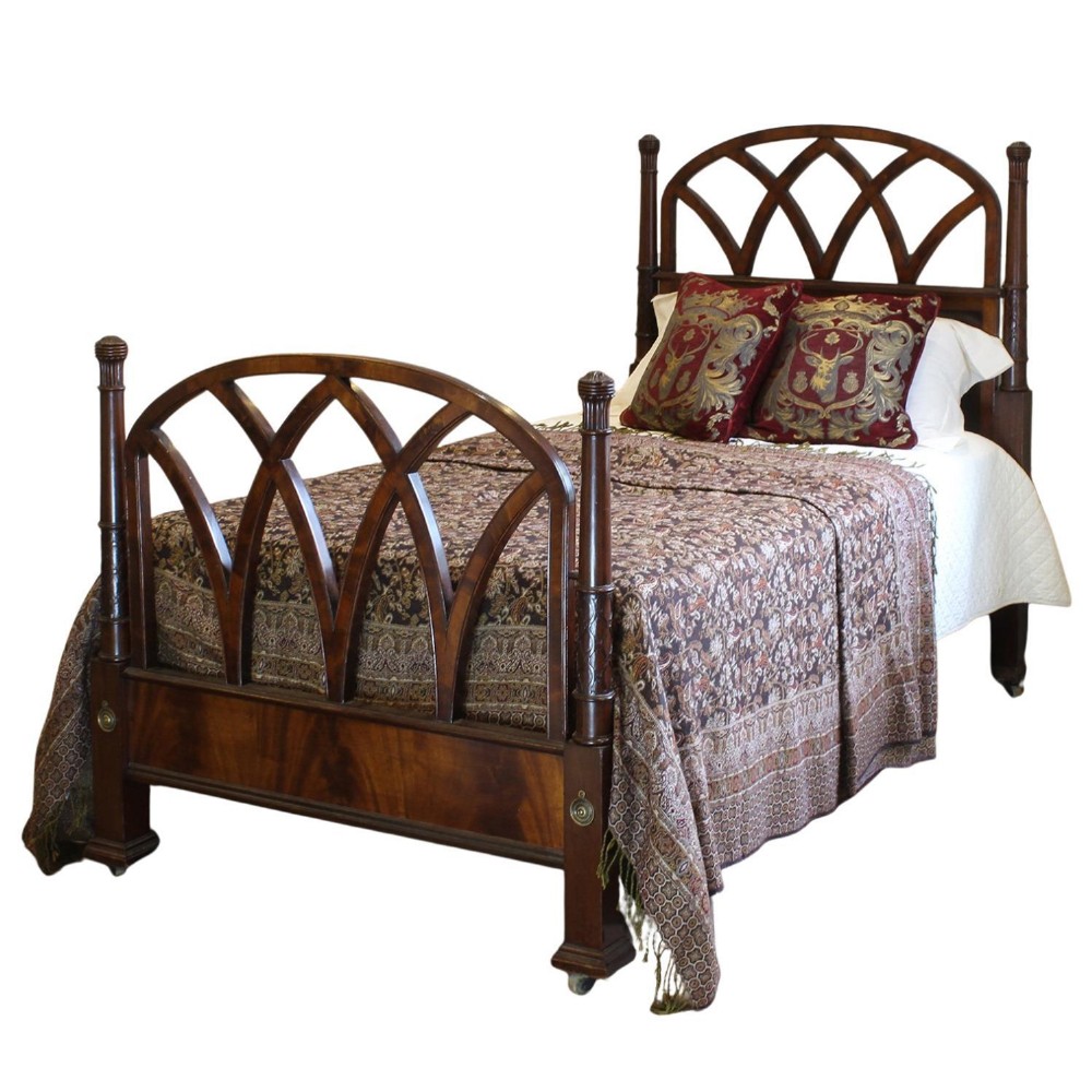 Antique dark mahogany single bedstead featuring Gothic pointed arch tracery on the headboard and footboard with turned posts and brass castors.