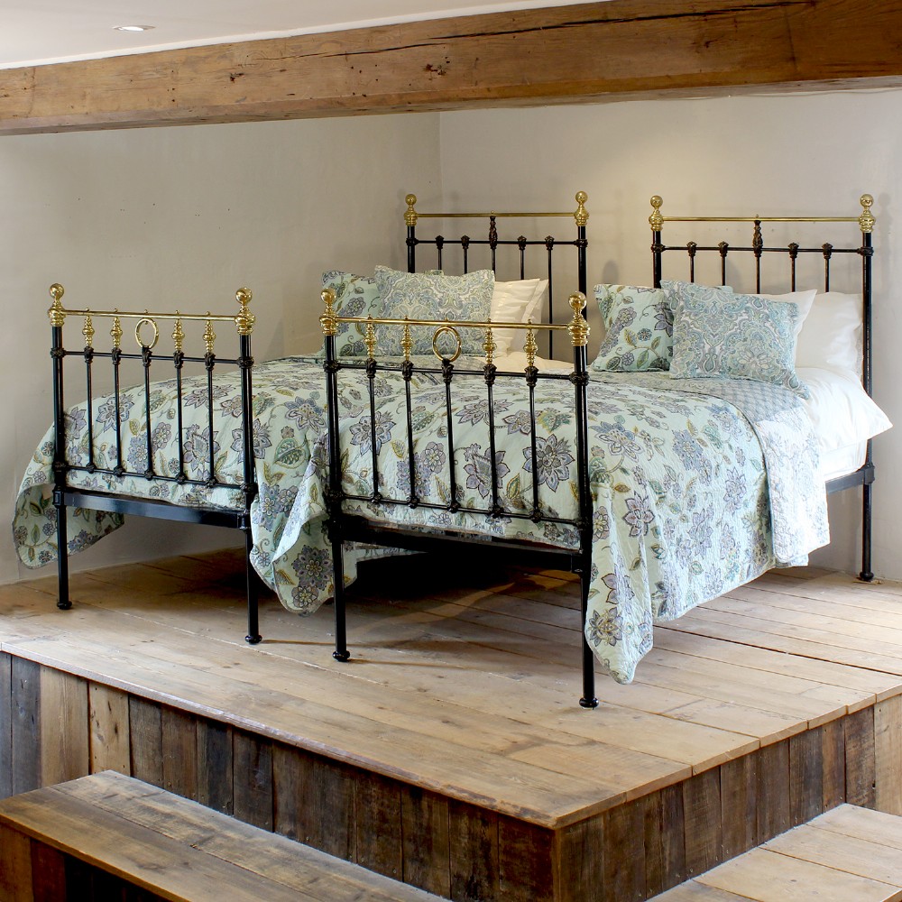 A matching pair of black cast iron single bed frames featuring vertical spindles and polished brass top rails with decorative finials.