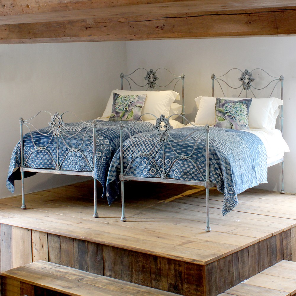 A matching pair of single cast iron beds featuring scrollwork headboards and footboards finished in a blue verdigris patina.
