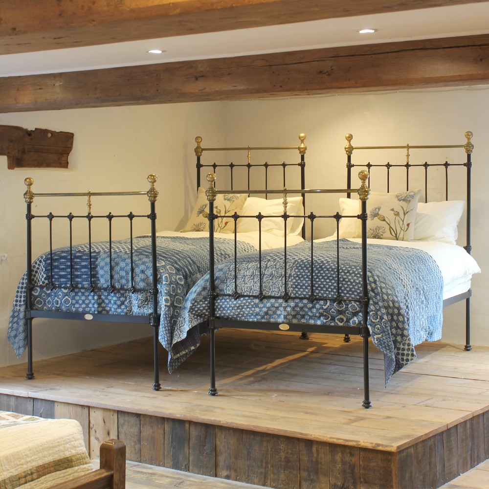 A matching pair of Victorian black cast iron single beds featuring vertical spindles and polished brass top rails with urn finials.
