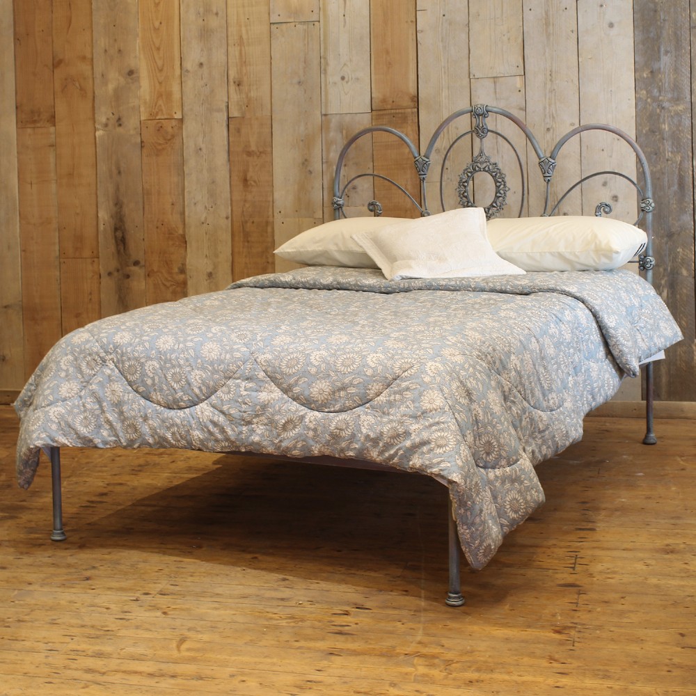 A double metal bed frame featuring an ornate wrought iron headboard with scrollwork detail and a distressed blue verdigris painted finish.